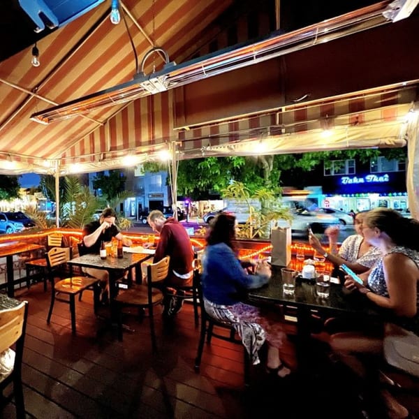 Patrons dining at night on an outdoor patio with a striped awning and string lights.