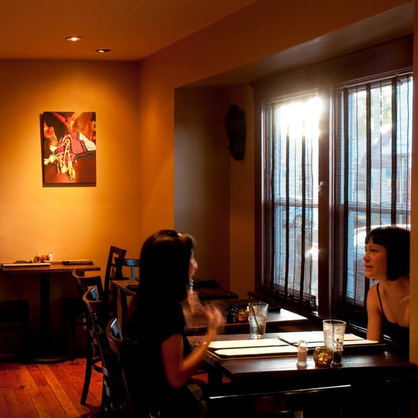 Two women dining at Muzita Abyssinian Bistro, bathed in warm light from a window.