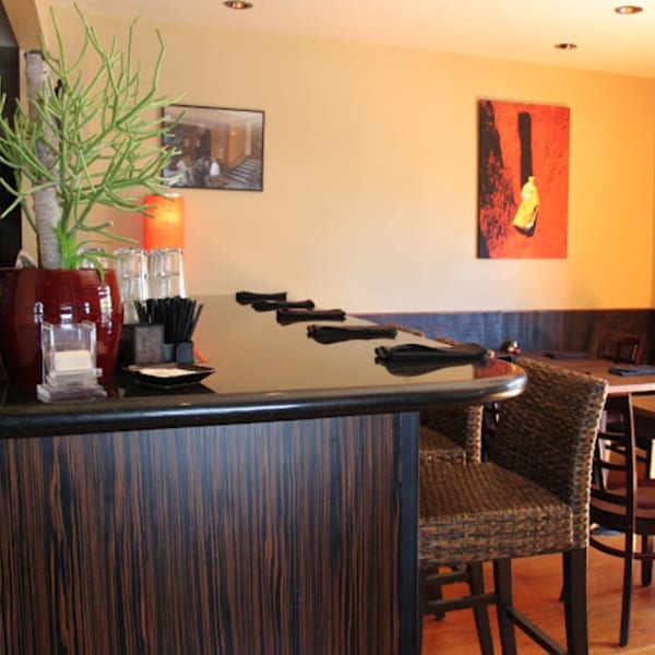 A modern bar area with dark wood, wicker chairs, and Ethiopian art on the light-colored walls.