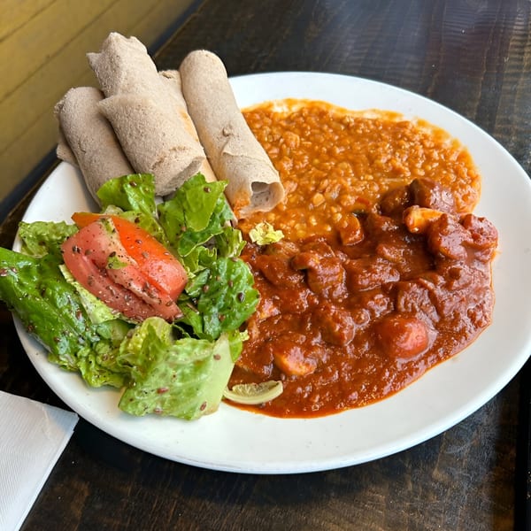Ethiopian dish with injera bread, red lentil stew, chicken wat, and a side salad.