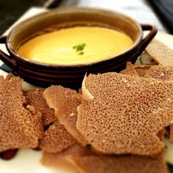 Ethiopian shiro wot, a yellow stew, in a brown pot, surrounded by injera bread.