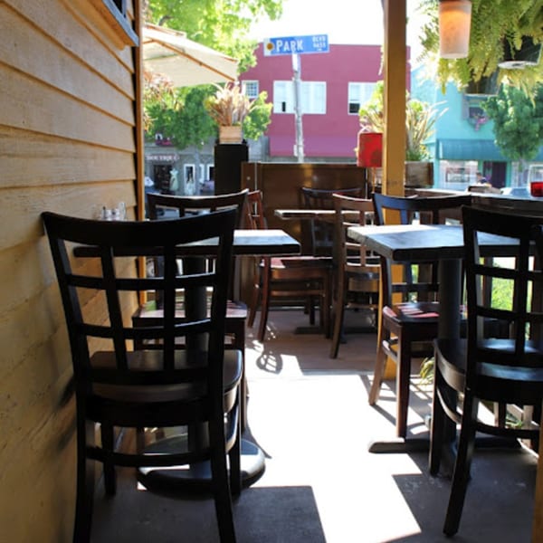 Outdoor patio seating area with wooden tables and chairs, bathed in sunlight, at Muzita Abyssinian Bistro.