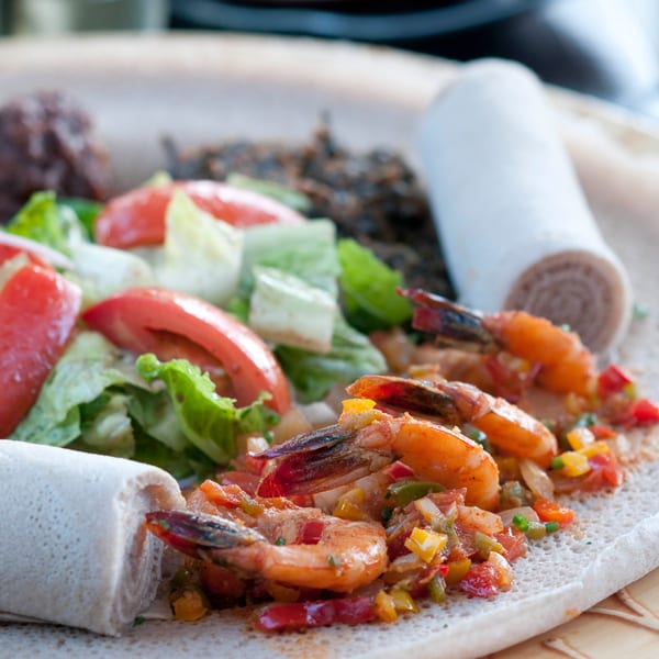 Ethiopian shrimp dish with injera, salad, and other accompaniments on a large platter.