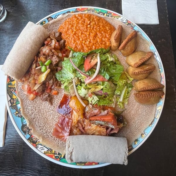 A colorful Ethiopian platter with injera, various stews, a fresh salad, and sambusas.