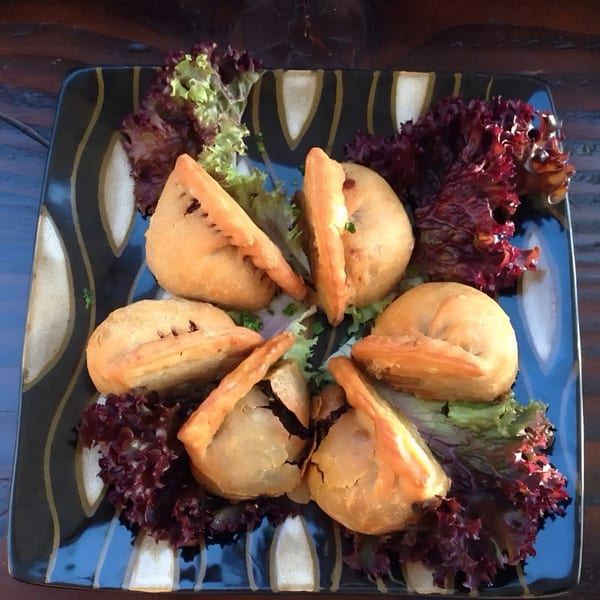 Six golden-brown Ethiopian sambusas, some split open, arranged on a bed of red and green lettuce.