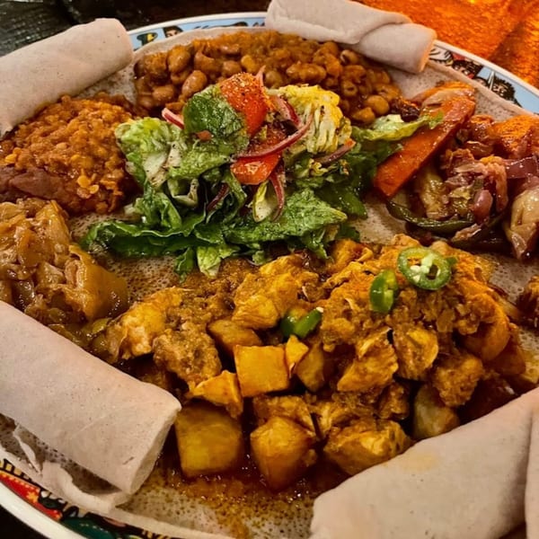 A colorful platter of Ethiopian food, including injera, lentils, chicken, vegetables, and salad.