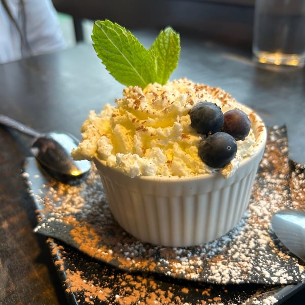 Dessert in a white ramekin, topped with whipped cream, blueberries, mint, and cocoa powder.