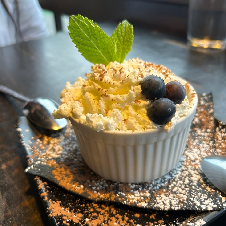Dessert in a white ramekin, topped with whipped cream, blueberries, mint, and cocoa powder.