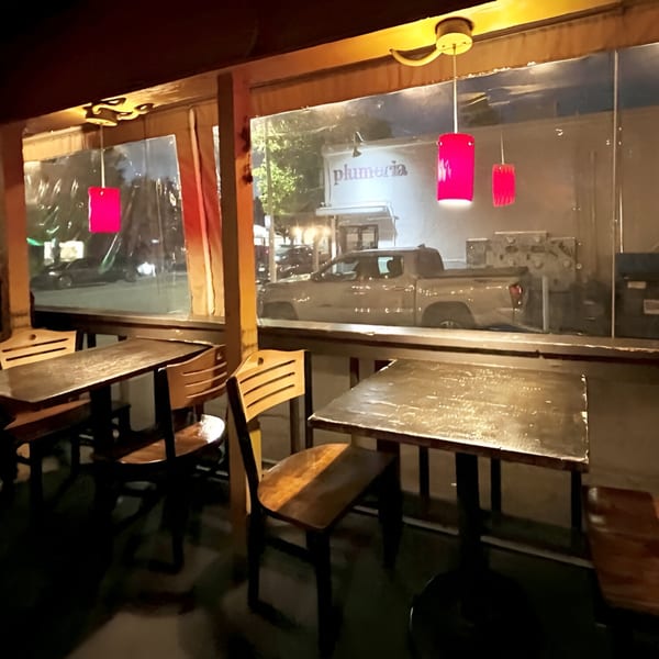 Empty outdoor dining area at Muzita Abyssinian Bistro with wooden tables and chairs, illuminated by pink lights.