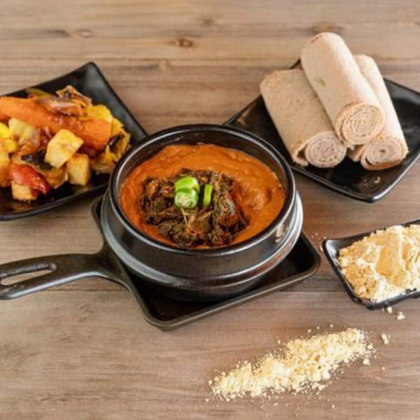 Ethiopian dishes: a stew in a black pot, injera rolls, and a vegetable mix on a wooden table.